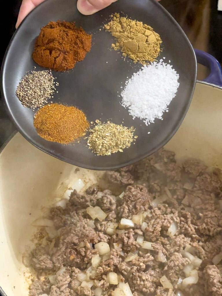 Spices being added to cooked ground beef and onions.