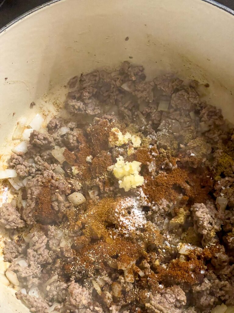 Spices on top of cooked ground beef and onions in a dutch oven.