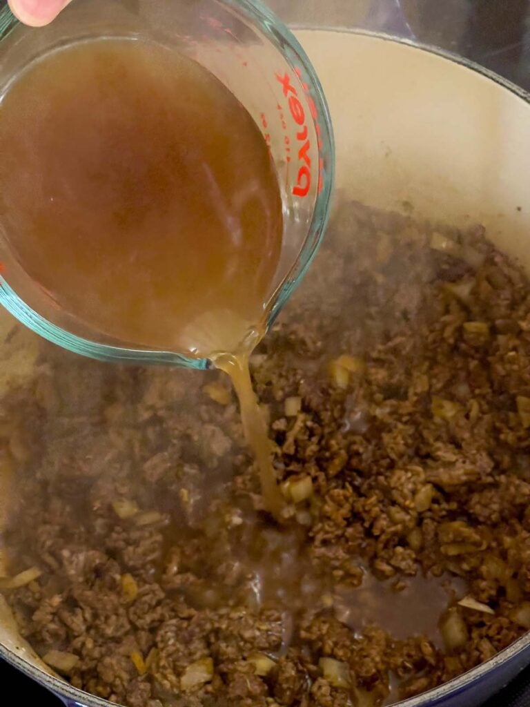 Beef broth being added to cooked ground beef.