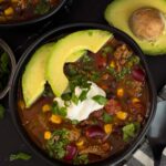 Bowls of taco soup in dark bowls with many garnishes.