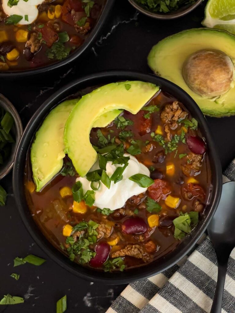 Bowls of taco soup in dark bowls with many garnishes.