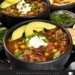 Bowls of taco soup in dark bowls with many garnishes.