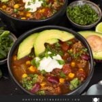 Bowls of taco soup in dark bowls with many garnishes.