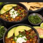 Bowls of taco soup in dark bowls with many garnishes.