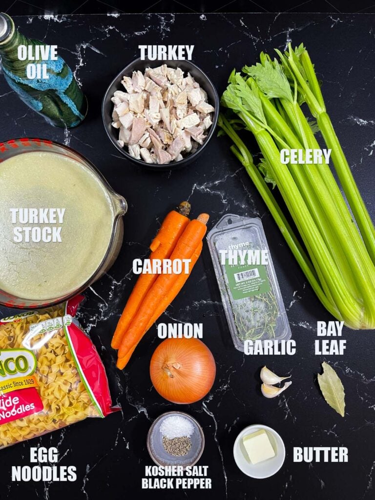 Ingredients for turkey noodle soup recipe on a dark surface.
