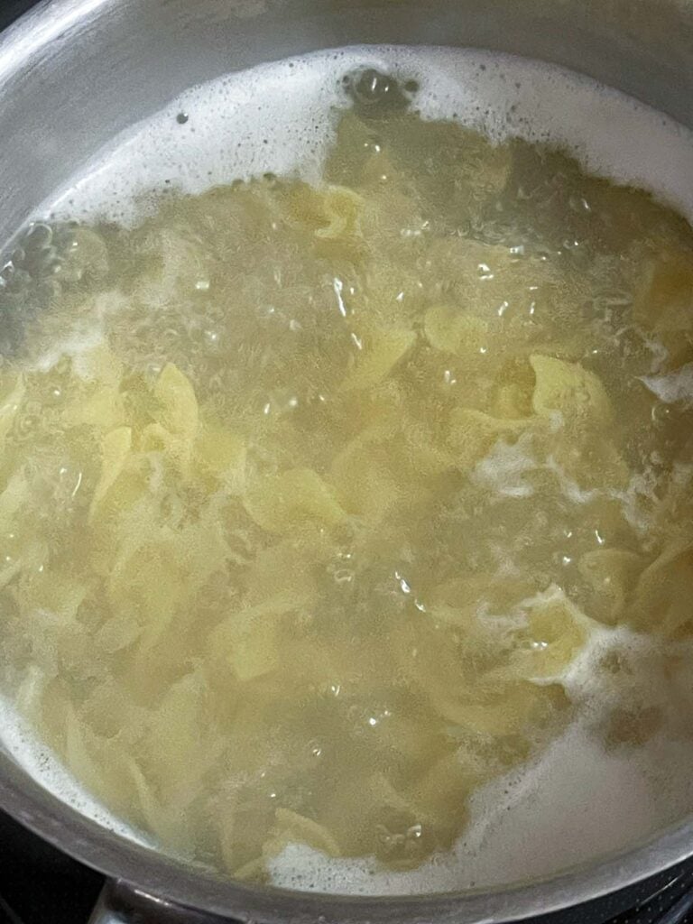 Wide egg noodles boiling in a pot for turkey noodle soup.
