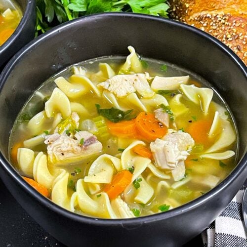 Turkey noodle soup in a dark round bowl.