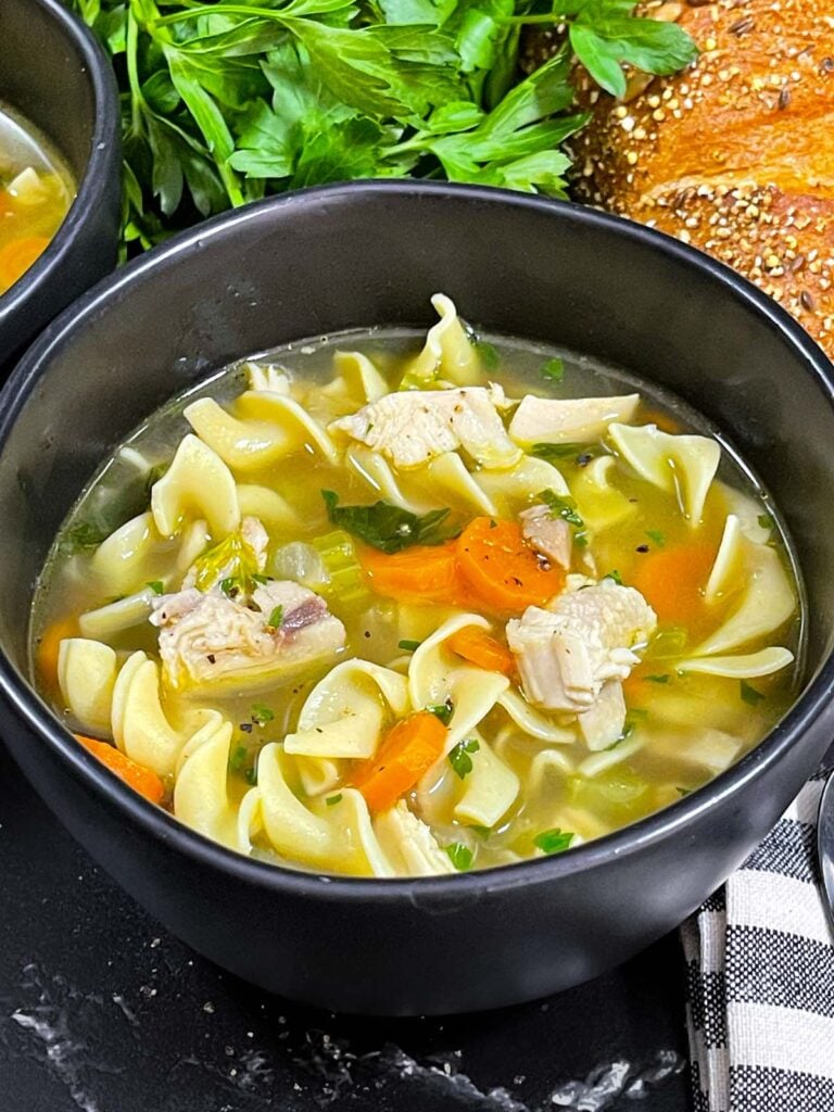 Turkey noodle soup in a dark round bowl.