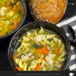 Two dark bowls of turkey noodle soup on a dark surface.