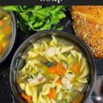 Two dark bowls of turkey noodle soup on a dark surface.