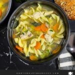 Two dark bowls of turkey noodle soup on a dark surface.