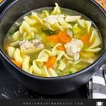 Two dark bowls of turkey noodle soup on a dark surface.