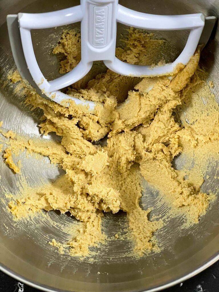 Butter and sugars creamed together in a metal mixing bowl.
