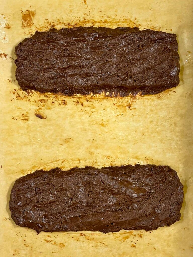 Chocolate peppermint biscotti formed into two logs on a parchment paper lined baking sheet.