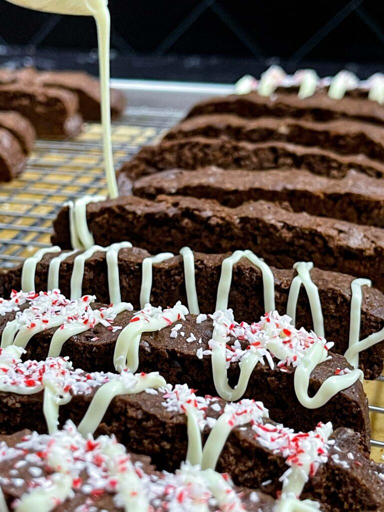 White chocolate being drizzled over the biscotti and garnished with crushed peppermint.