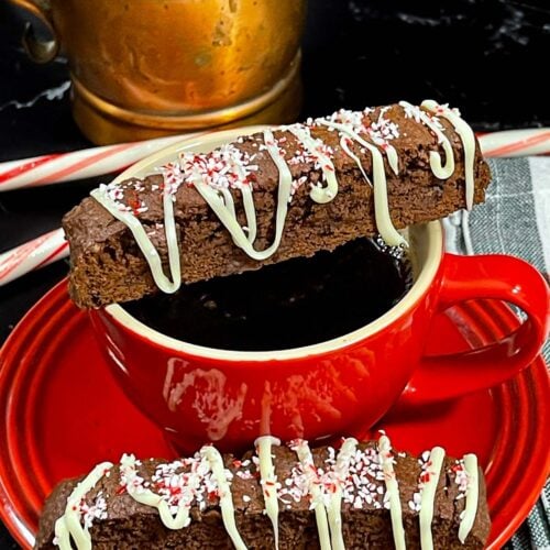 A slice of chocolate peppermint biscotti place over a cup of coffee with another slice on the saucer.
