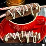 A slice of chocolate peppermint biscotti place over a cup of coffee with another slice on the saucer.