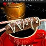 A slice of chocolate peppermint biscotti place over a cup of coffee with another slice on the saucer.