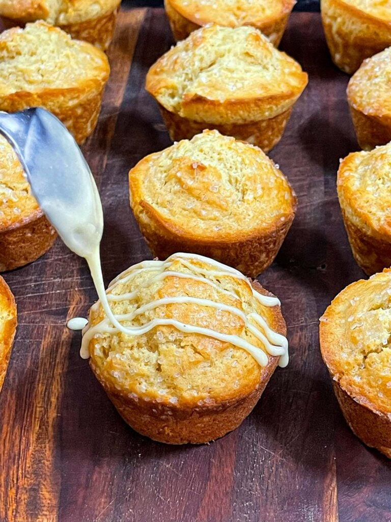 Eggnog glaze being drizzled over the muffins on a wooden board.