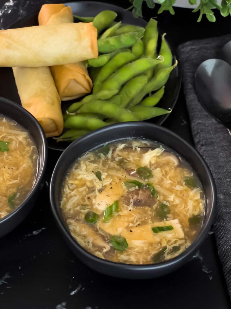 Hot and sour soup in dark bowls on a dark surface.