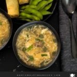 Hot and sour soup in a dark bowl on a dark surface.
