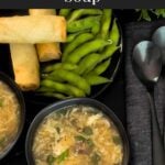 Hot and sour soup in a dark bowl on a dark surface.