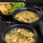 Hot and sour soup in a dark bowl on a dark surface.
