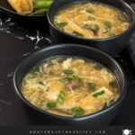 Hot and sour soup in a dark bowl on a dark surface.
