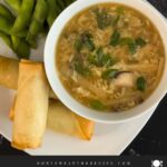 Hot and sour soup in a light bowl on a square plate with edamame and spring rolls.