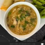 Hot and sour soup in a light bowl on a square plate with edamame and spring rolls.