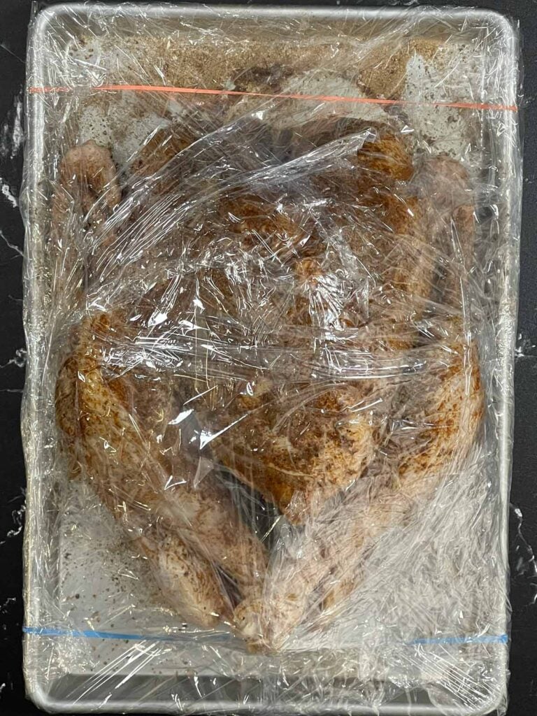 A dry brined raw turkey on a baking sheet.