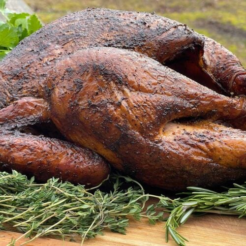 A whole smoked turkey on a wooden cutting board with fresh herbs.