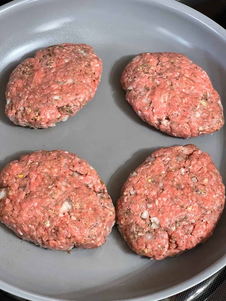 Salisbury steak patties cooking in a skillet before browning