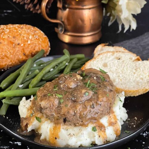 Close-up of Salisbury steak with mushroom gravy pouring over mashed potatoes