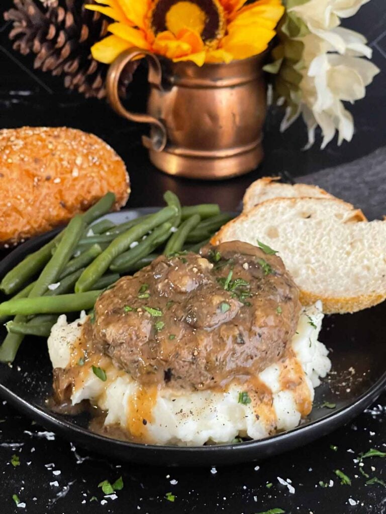 Close-up of Salisbury steak with mushroom gravy pouring over mashed potatoes