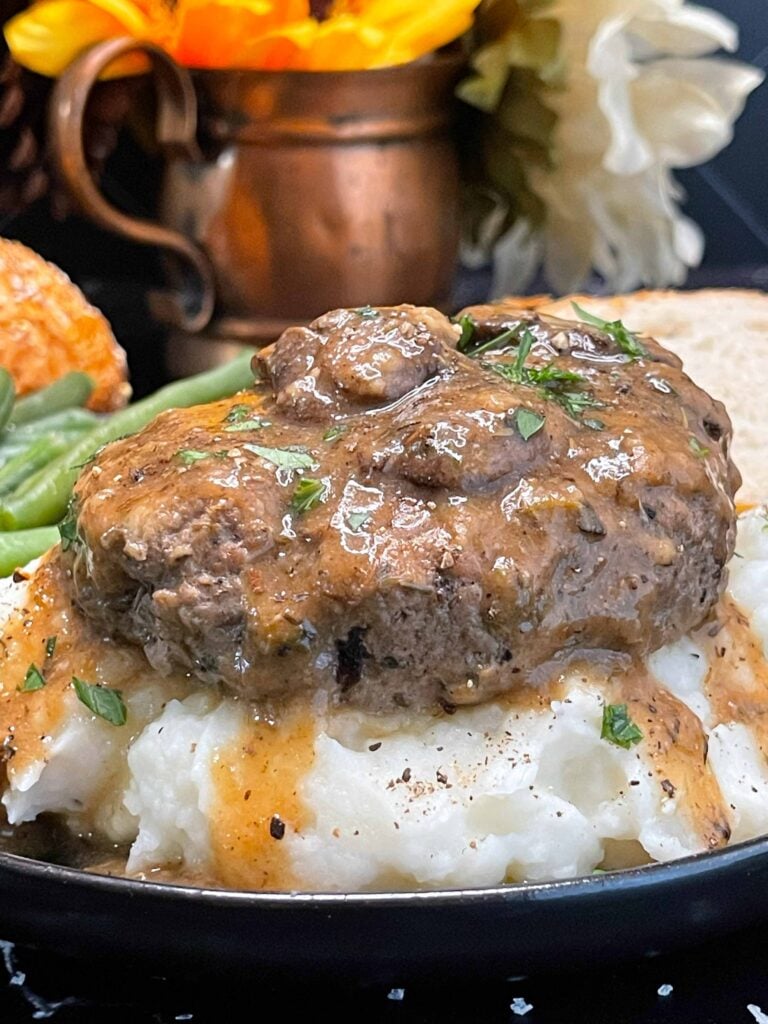 Close-up of Salisbury steak with mushroom gravy pouring over mashed potatoes