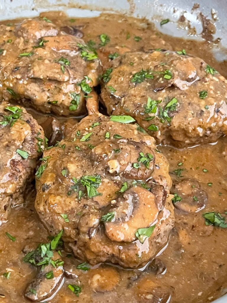 Salisbury steak simmering in mushroom gravy in a skillet, garnished with fresh parsley