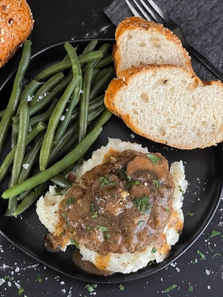 Salisbury steak with mushroom gravy served over mashed potatoes with green beans and bread