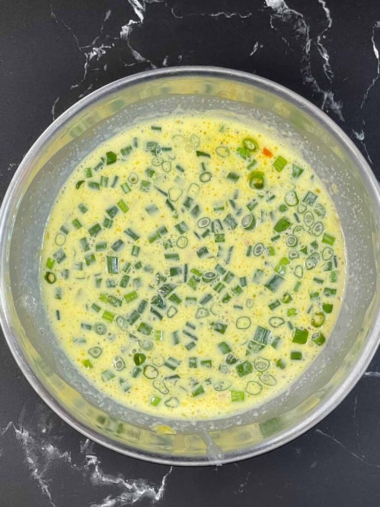 Cooked bell peppers and green onions added to an egg mixture whisked together.