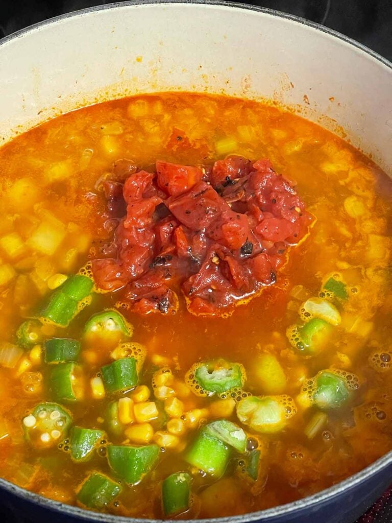 Adding more vegetables to a cooking Brunswick stew.