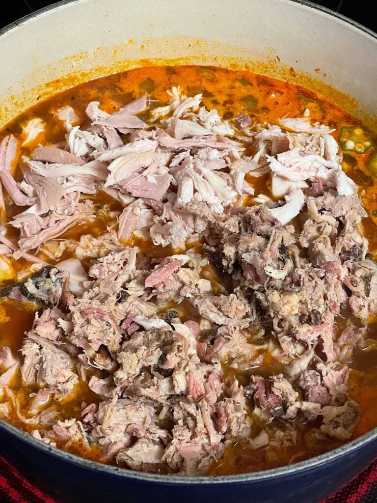 Adding smoked meat to the Brunswick stew base.