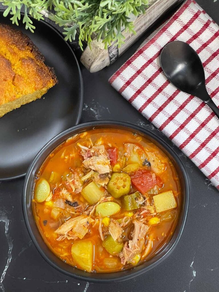 Brunswick Stew in a dark bowl with cornbread in the background.