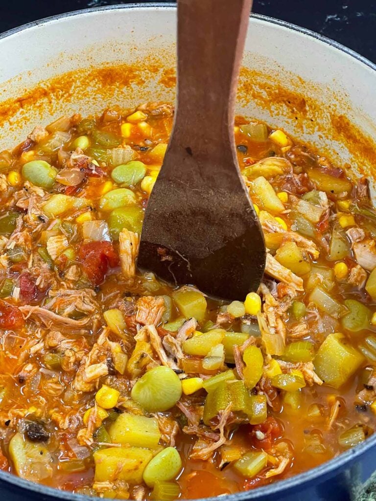 A wooden spoon standing in a pot of Brunswick Stew.