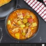 Brunswick Stew in a dark bowl with cornbread in the background.
