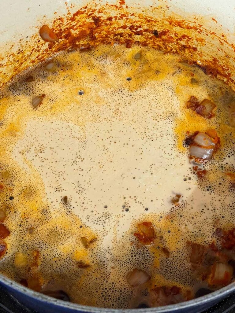 A Guinness beer added to ingredients in a dutch oven.