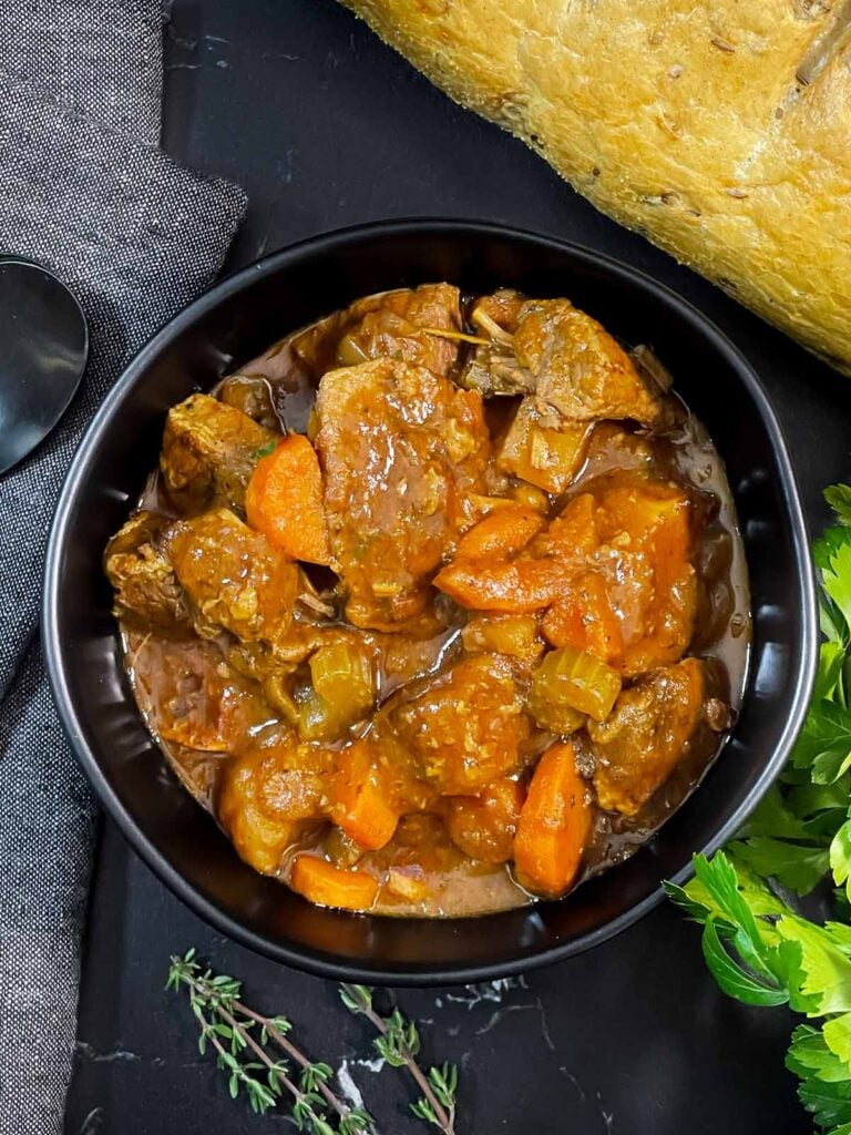 Guinness Beef Stew in a dark bowl with a bread and herb garnish.