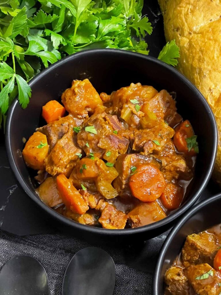 Guinness Beef Stew in a dark bowl with a bread and herb garnish.