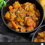 Guinness Beef Stew in a dark bowl with a bread and herb garnish.