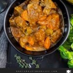 Guinness Beef Stew in a dark bowl with a bread and herb garnish.