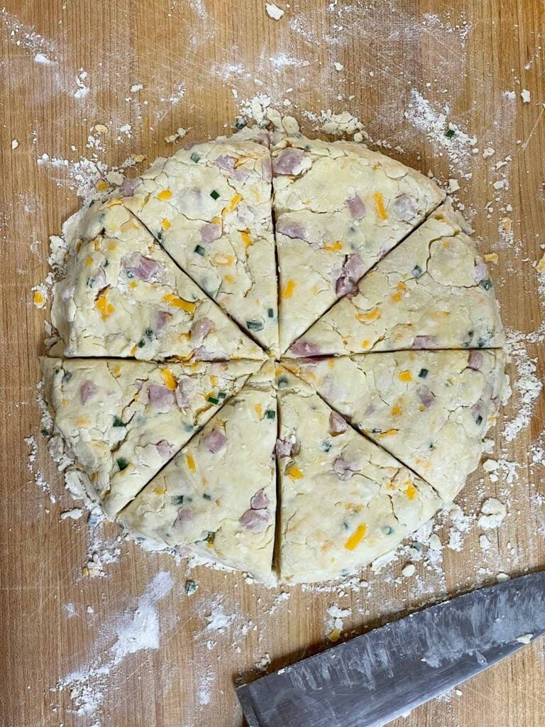 Ham and cheese scones dough cut into eight triangles on a wooden board.